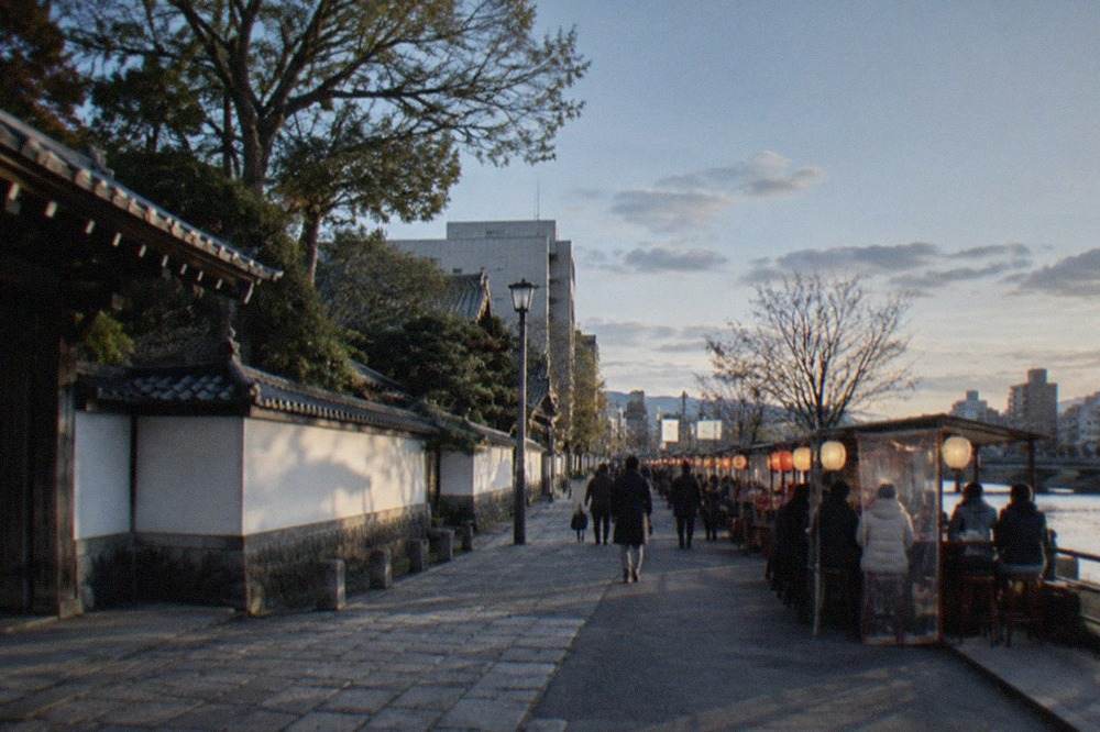 A lantern-lit food stall street beside a river in Fukuoka at dusk