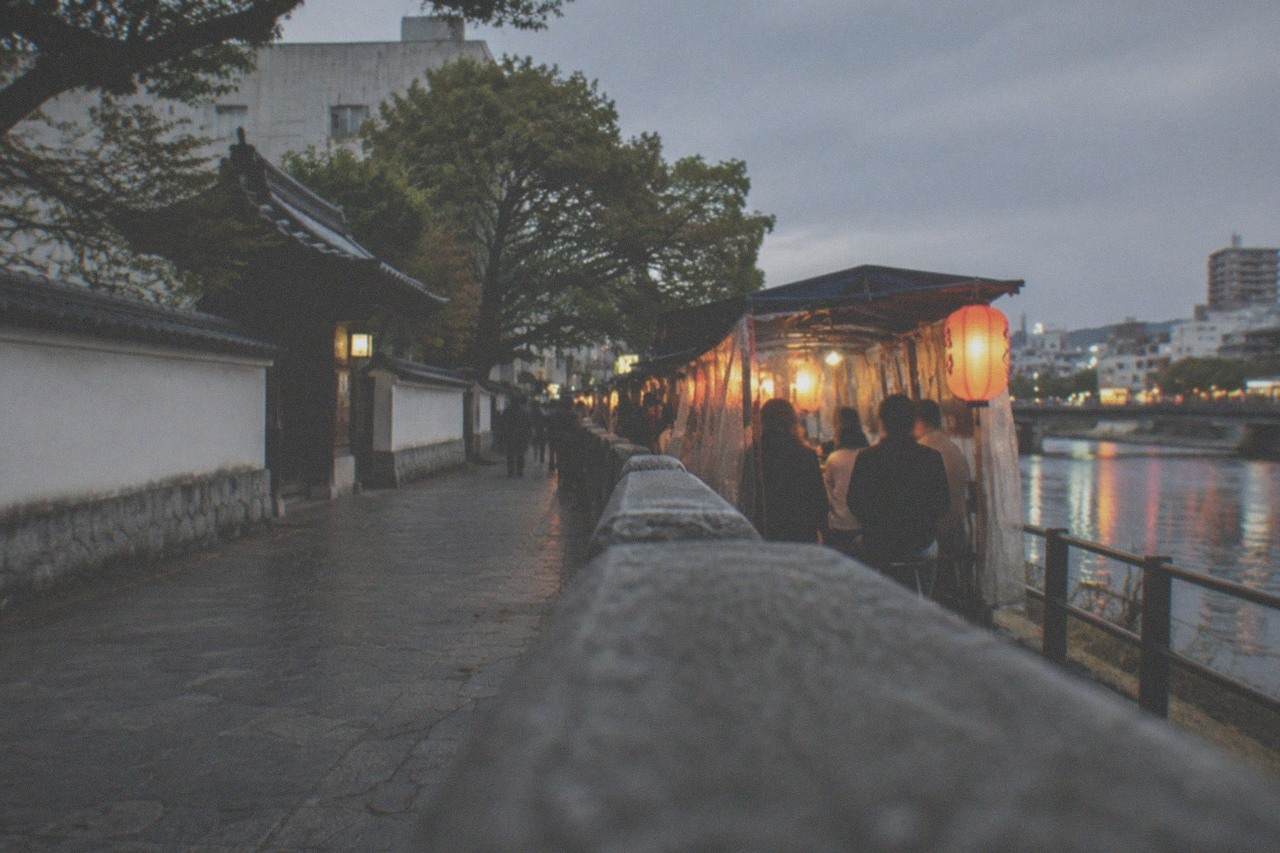 A lantern-lit food stall street beside a river in Fukuoka at dusk