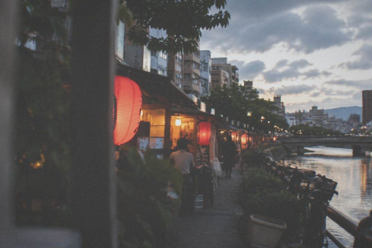 Evening food stalls with red lanterns lined up along a river in a Japanese city