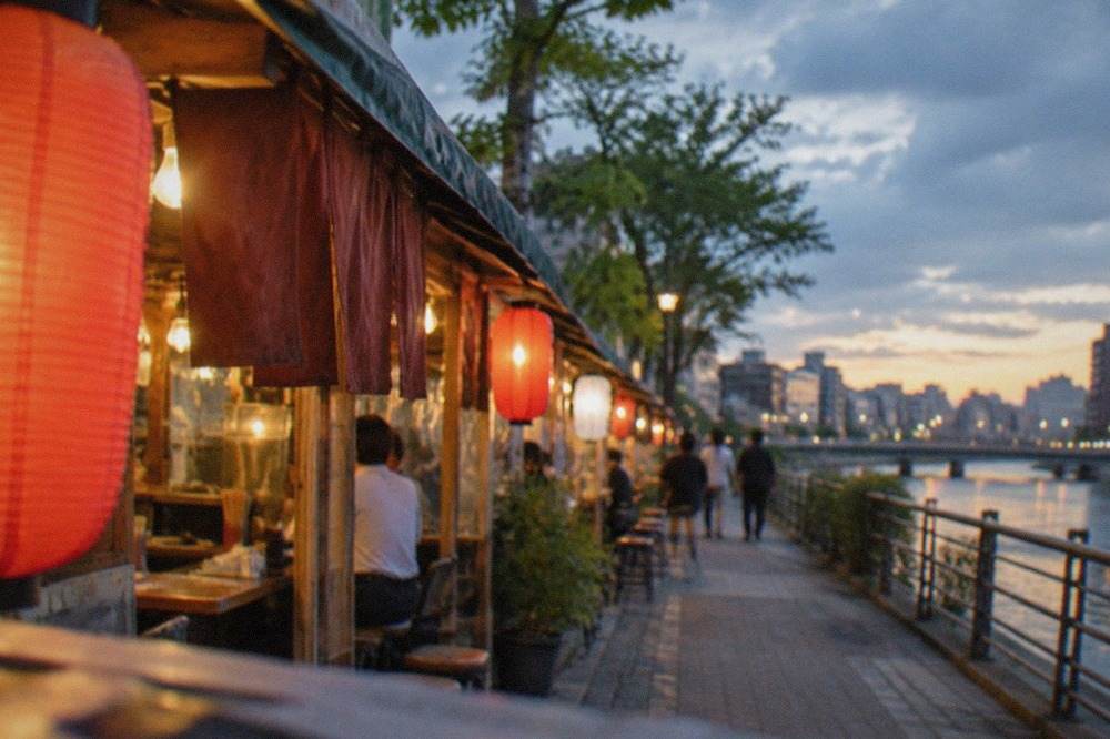 Food stalls with glowing lanterns lined along a riverside street at night in Fukuoka