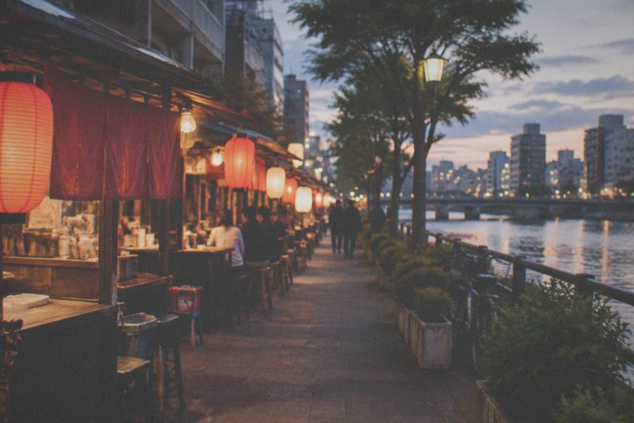 Food stalls with glowing lanterns lined along a riverside street at night in Fukuoka