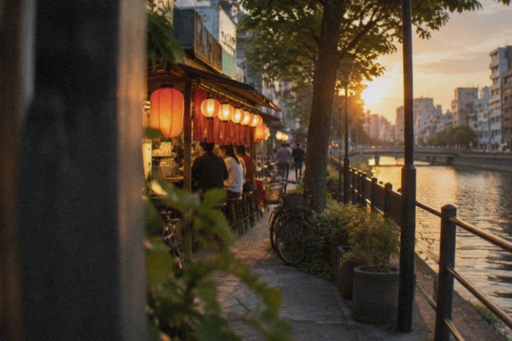 A canal-side street in Fukuoka with low-rise buildings and an evening food stall glowing under lanterns