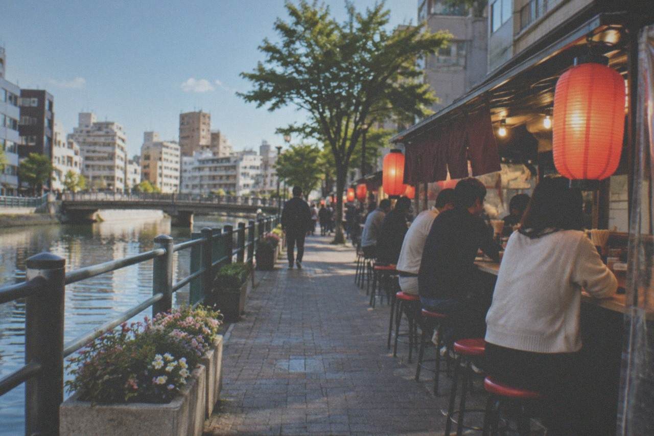 A canal-side street in Fukuoka with low-rise buildings and an evening food stall glowing under lanterns