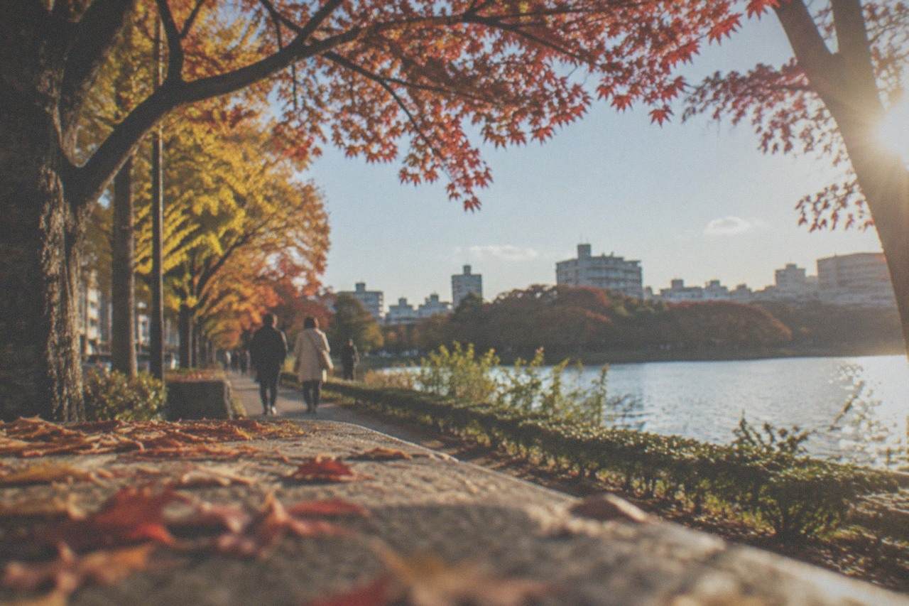 Ginkgo and maple trees with autumn colour along a park path beside a calm lake in Fukuoka