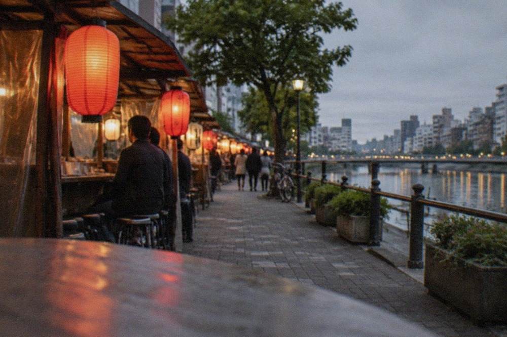 Evening food stalls with lanterns glowing along a riverside street in a Japanese city