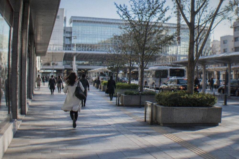 Hakata Station's modern glass facade above the surrounding city blocks under a clear sky