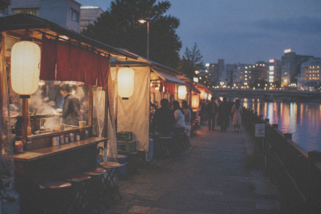 Row of glowing yatai food stalls lined up along a riverside street at night