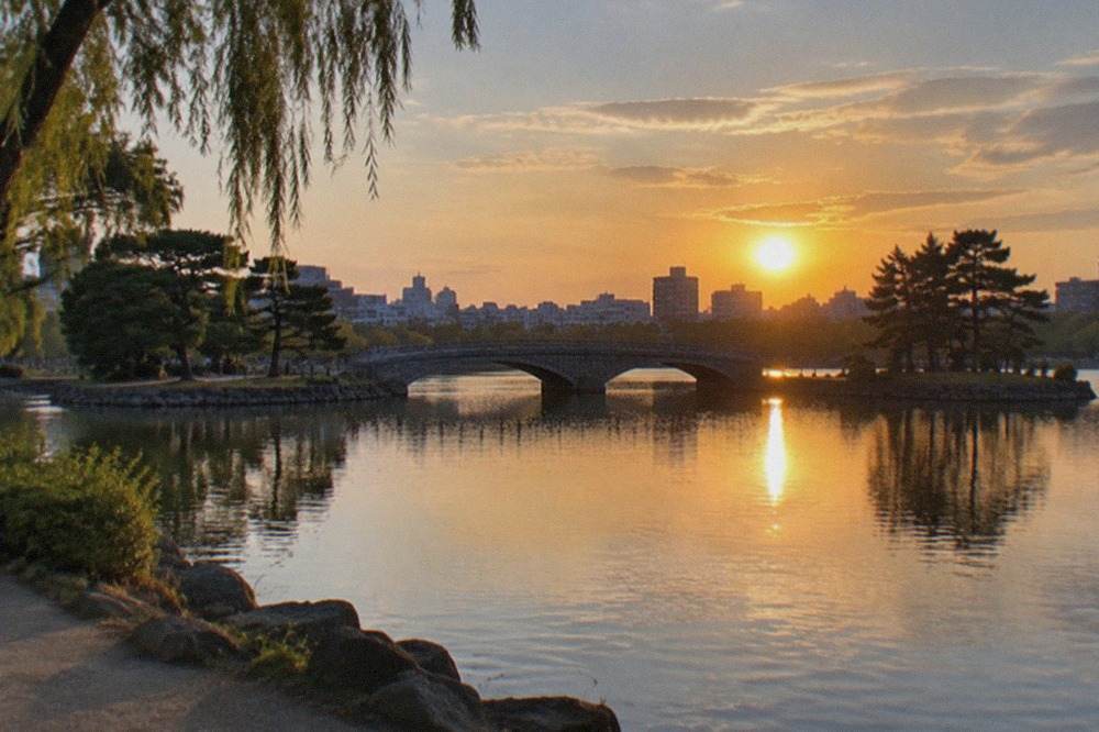 Ohori Park lake at sunset with the city skyline and a stone bridge across calm water