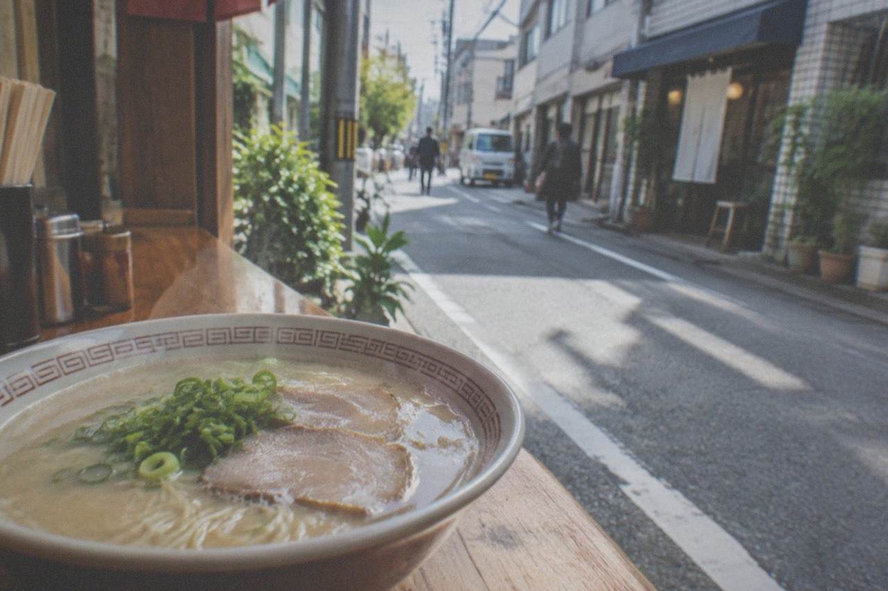 A steaming bowl of tonkotsu ramen with thin noodles, sliced pork and green onion on a wooden counter