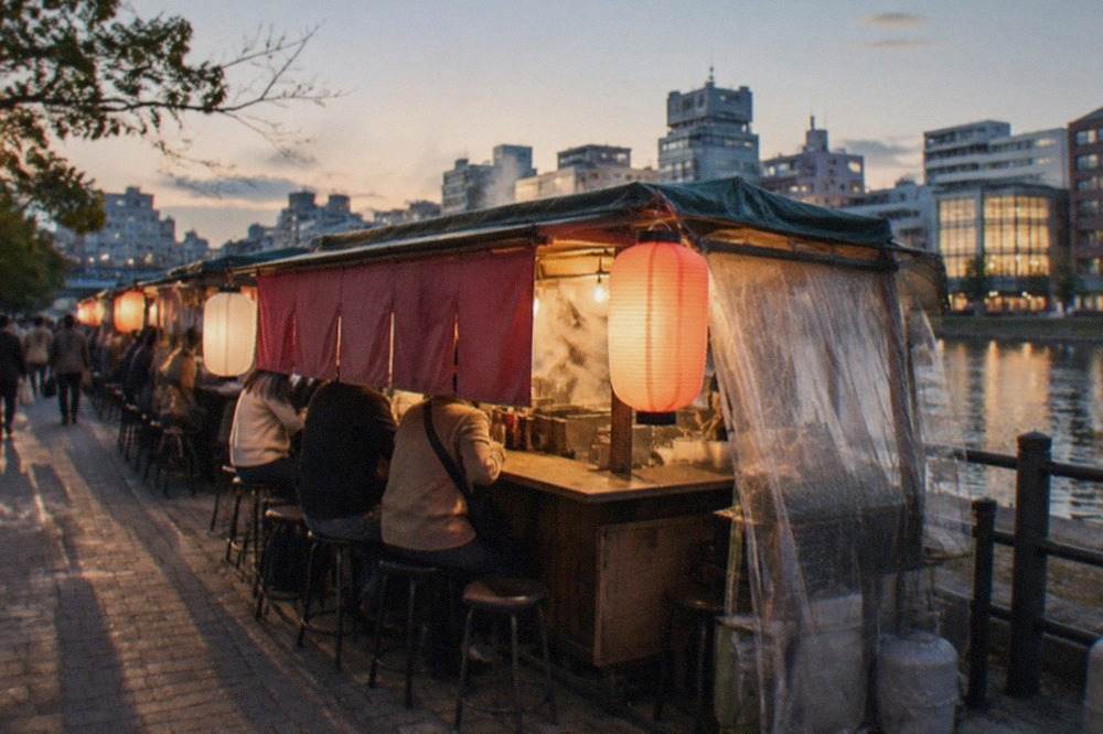 A small ramen stall glowing with lantern light on a city sidewalk at night