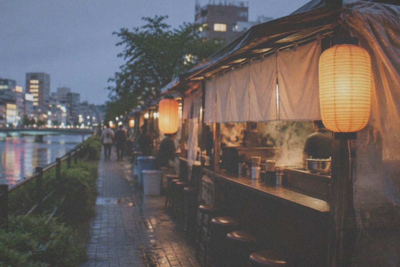 A small ramen stall glowing with lantern light on a city sidewalk at night