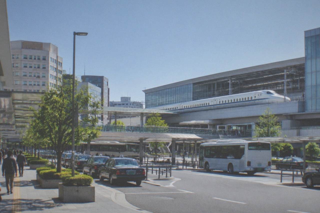 A Shinkansen bullet train waiting on a platform beside modern station buildings under a clear sky
