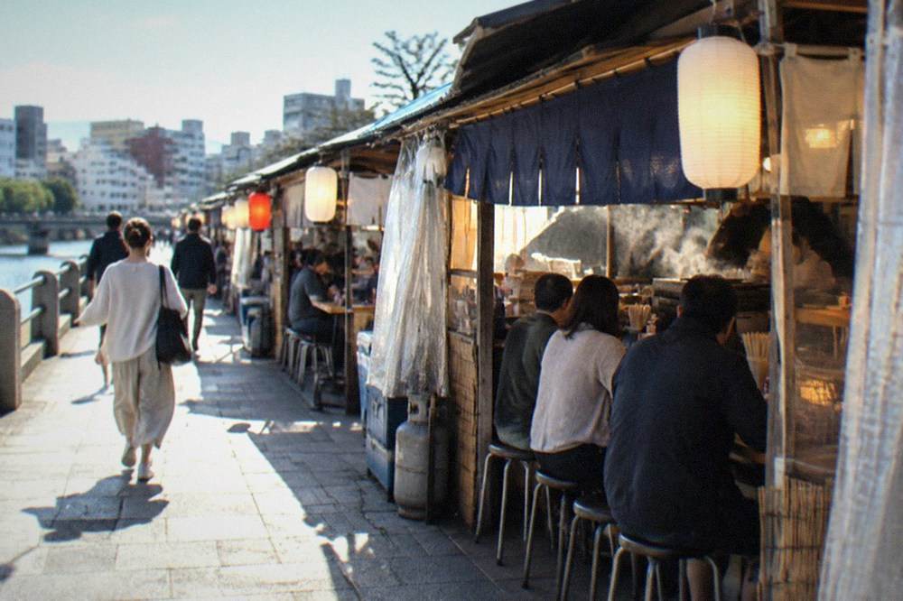 A lit yatai food stall at night with a counter of seated customers
