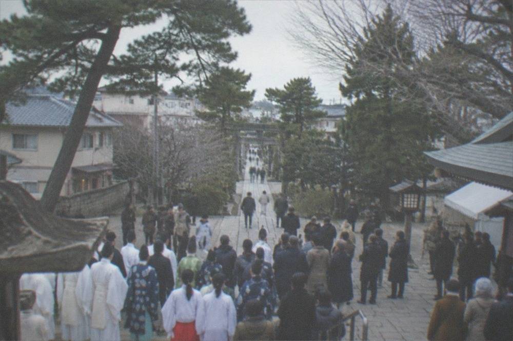 A crowd of festival participants in traditional dress gathered on the stone forecourt of a shrine in winter