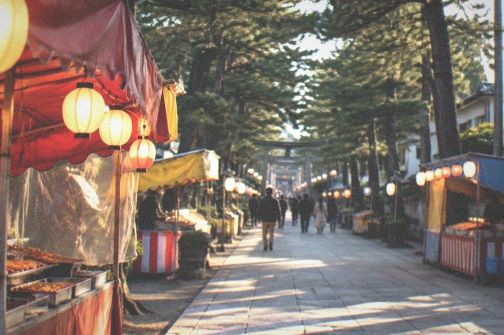 Rows of festival food stalls with paper lanterns lighting a shrine approach at dusk