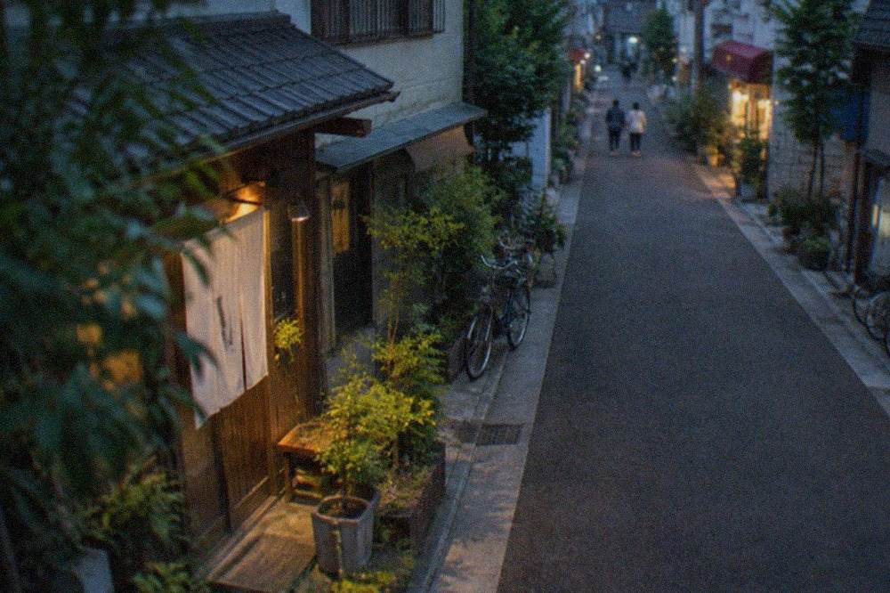 A quiet residential street in Imaizumi with small storefronts and greenery along the sidewalk