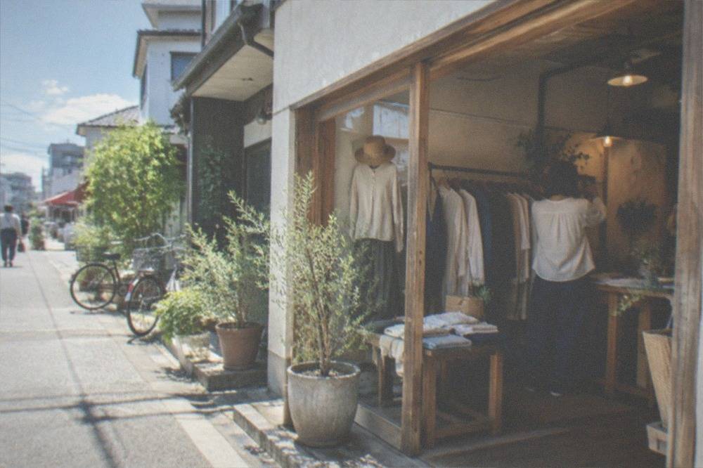 A single-room boutique in Imaizumi with clothing racks and a shopkeeper arranging a display
