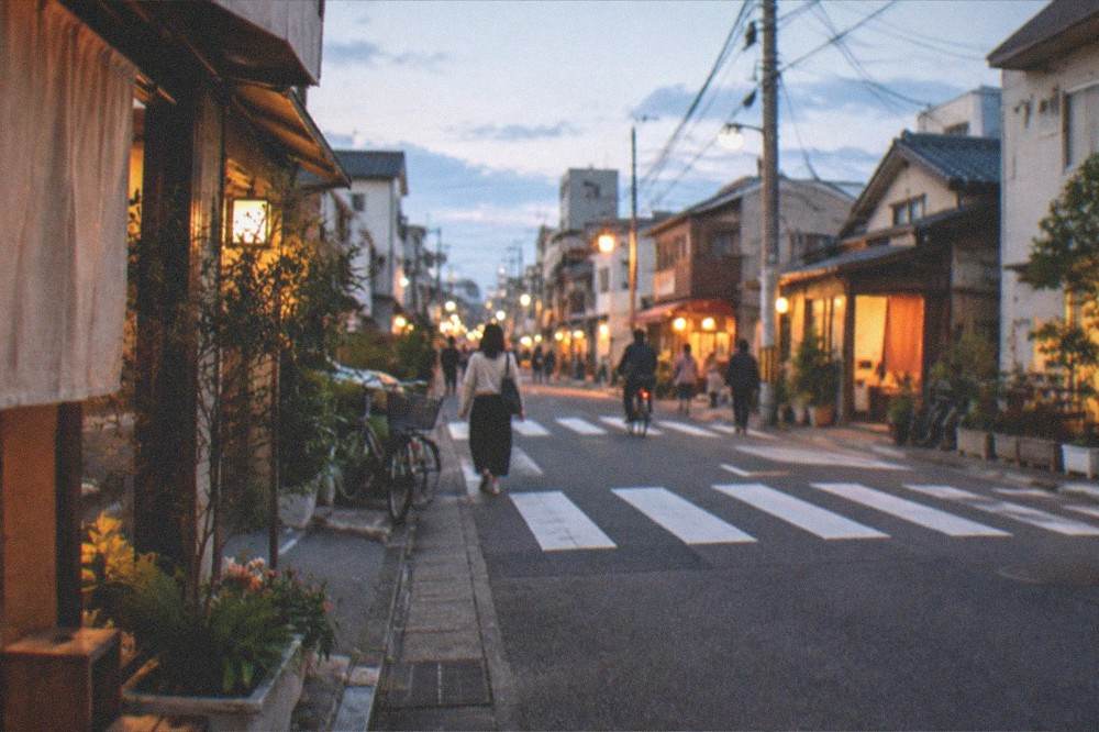 A pedestrian crossing in Imaizumi at dusk with warm light from small shop windows