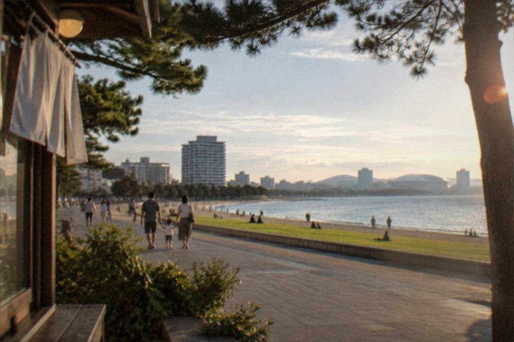 A wide seaside promenade with lawns and palm trees, families walking on a calm afternoon