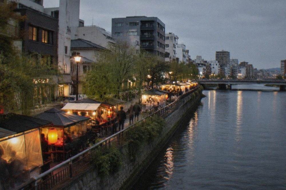Illuminated riverside food stalls glowing beside dark river water at night
