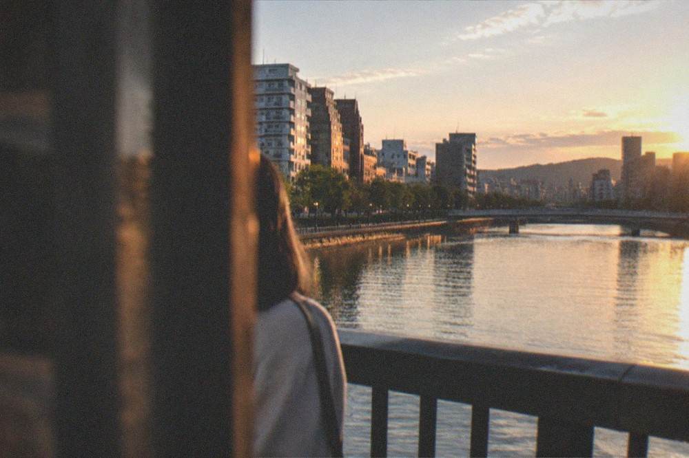 A modern city skyline at dusk seen across a river from a bridge