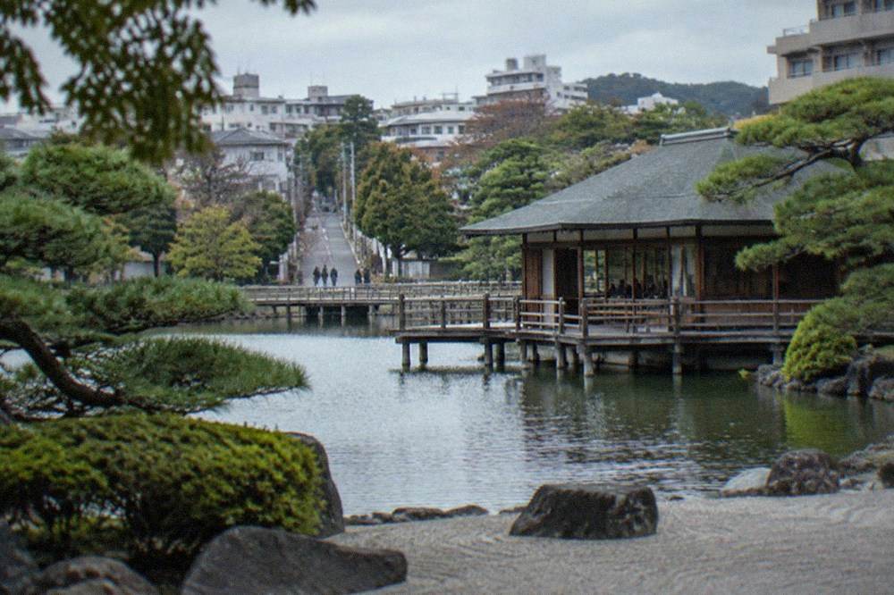 A raked gravel garden with clipped pines and a wooden pavilion beside a pond