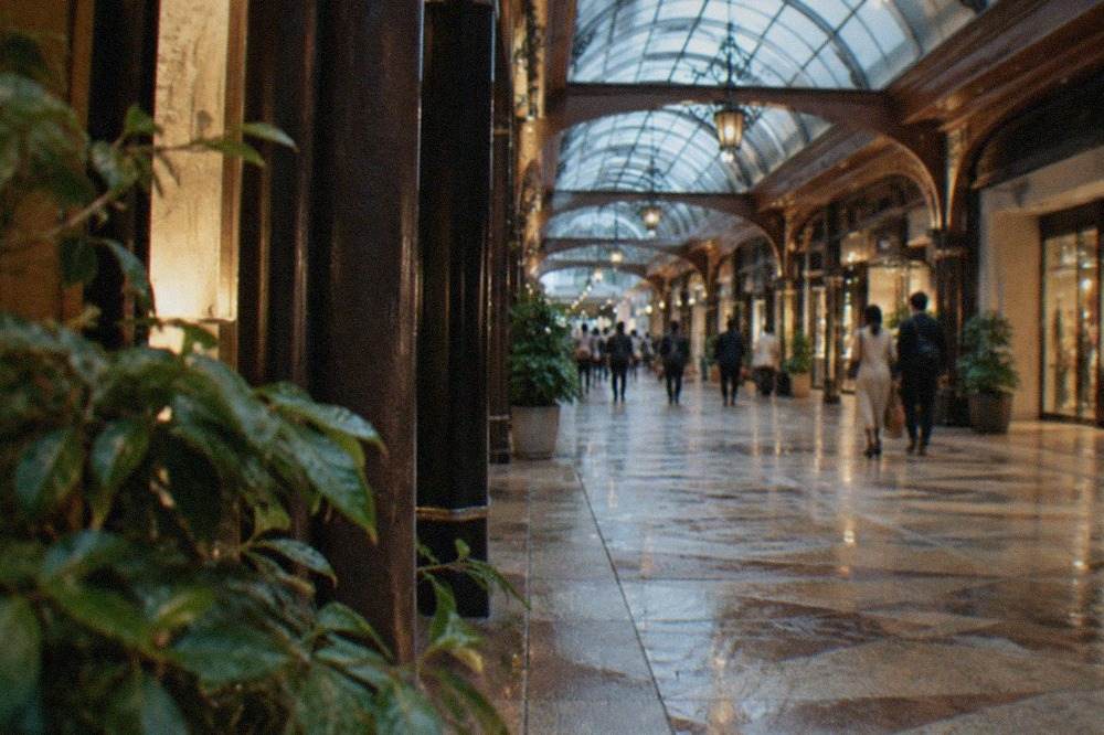 Glass-roofed underground shopping corridor with storefronts, polished floor, and soft lighting