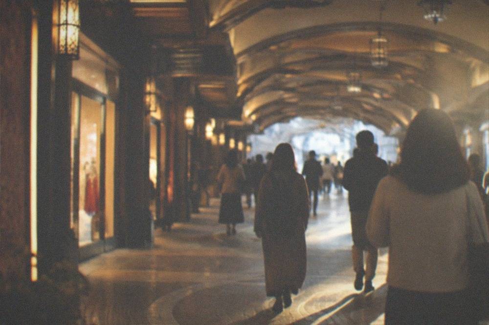 Shoppers walking through an underground retail passage with illuminated storefronts and shaded ceiling