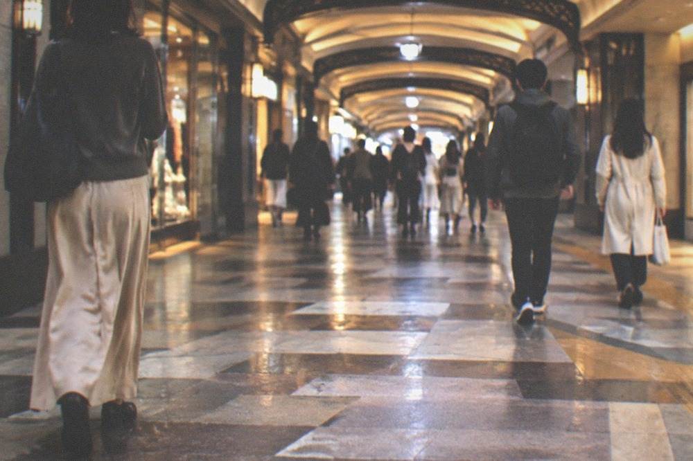 Underground mall intersection with tiled floor, surrounding shopfronts, and commuters passing