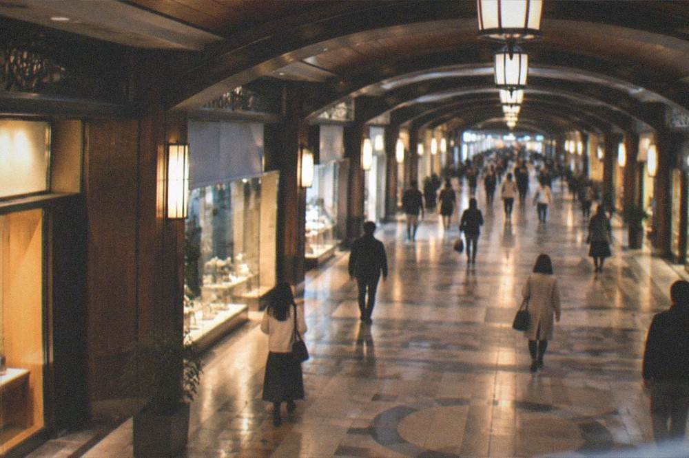 Wide underground mall corridor with overhead lights, polished floor, and small shops along both sides