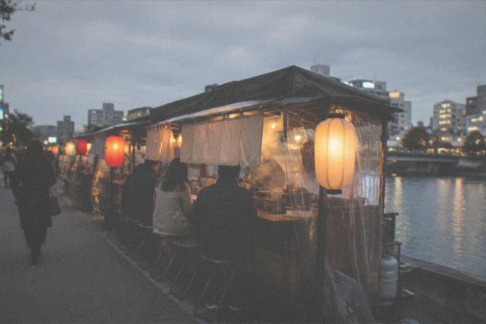 A yatai food stall glowing at night beside a city street with a few seated customers