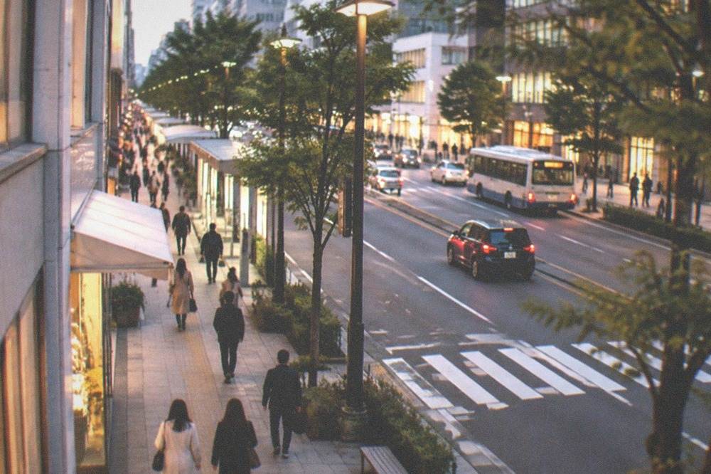 A city street in Tenjin at dusk with lit shopfronts and pedestrians walking