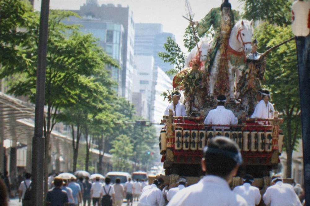 A festival float decorated with figures standing on a city street in summer