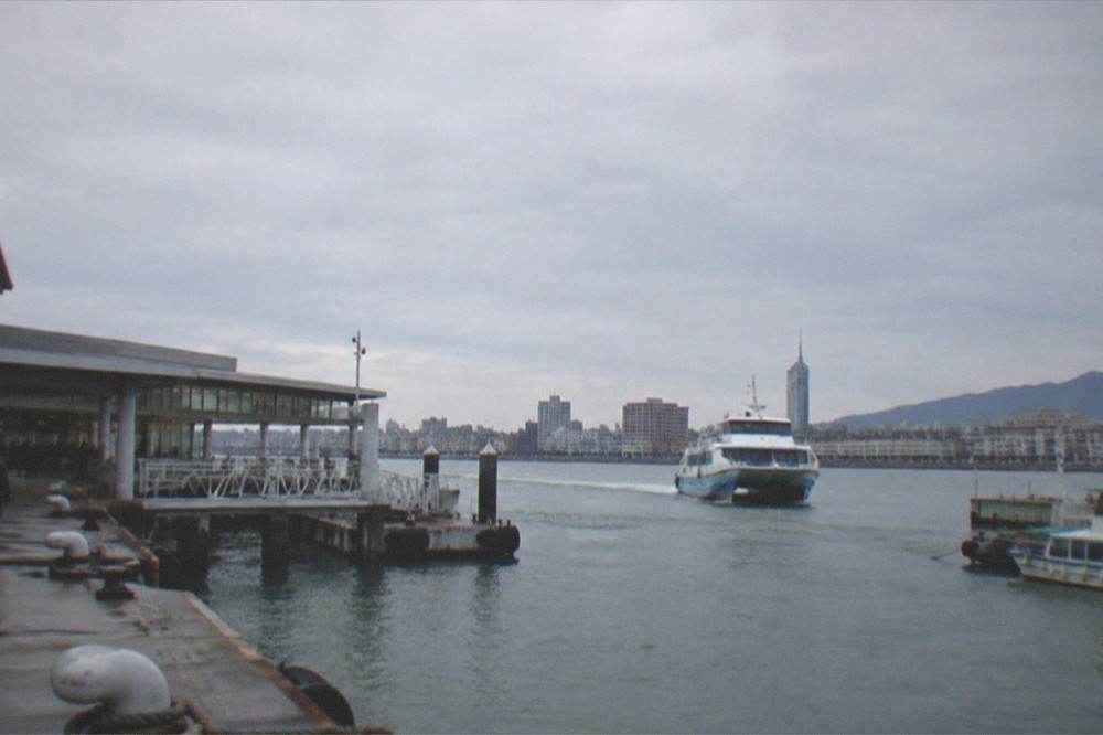 Ferry gliding into a harbour berth with a modern city skyline rising behind