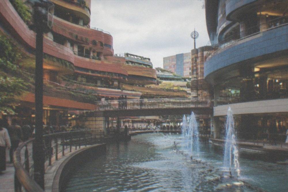 An indoor canal with walkways on both sides and shoppers crossing a small bridge