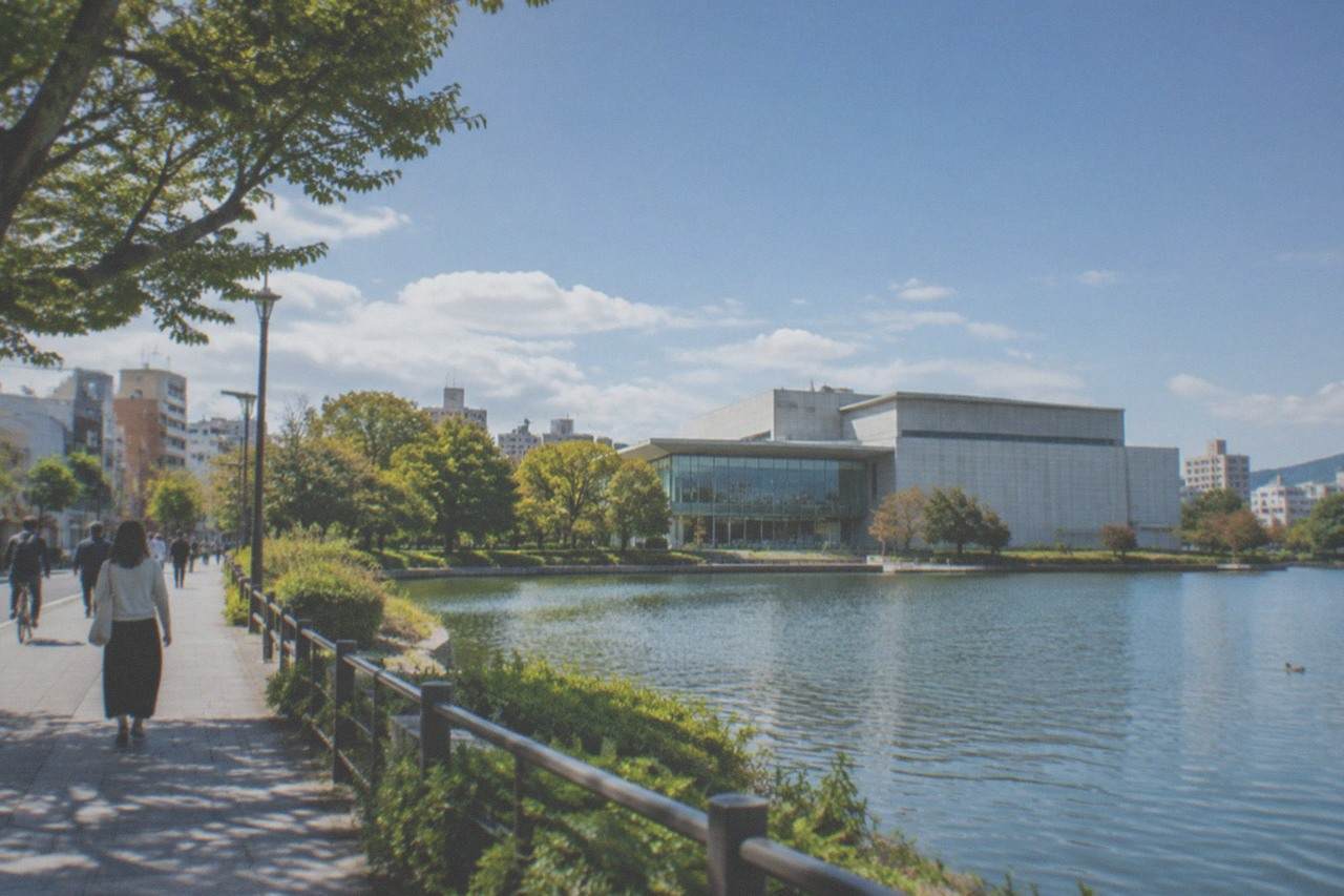 Modern museum building beside a calm park lake with trees along the waterfront