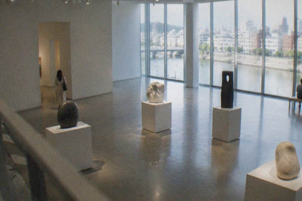 Museum gallery interior with contemporary sculptures displayed on pedestals under soft lighting
