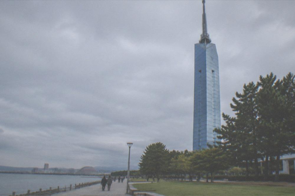 The lattice structure of Fukuoka Tower seen from below with mirror panels reflecting the sky
