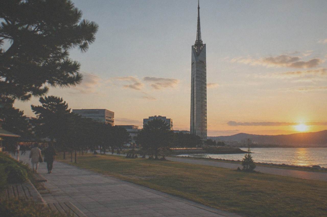 The silver lattice cylinder of Fukuoka Tower standing over the Momochi waterfront at dusk