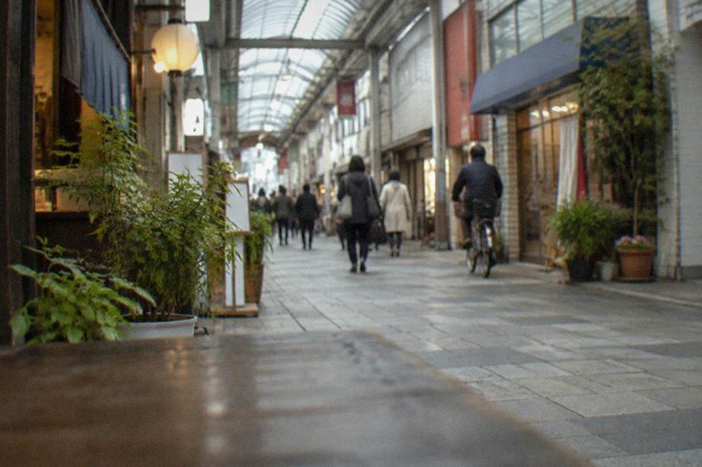A covered shopping arcade street with small shopfronts and hanging signs in Hakata.