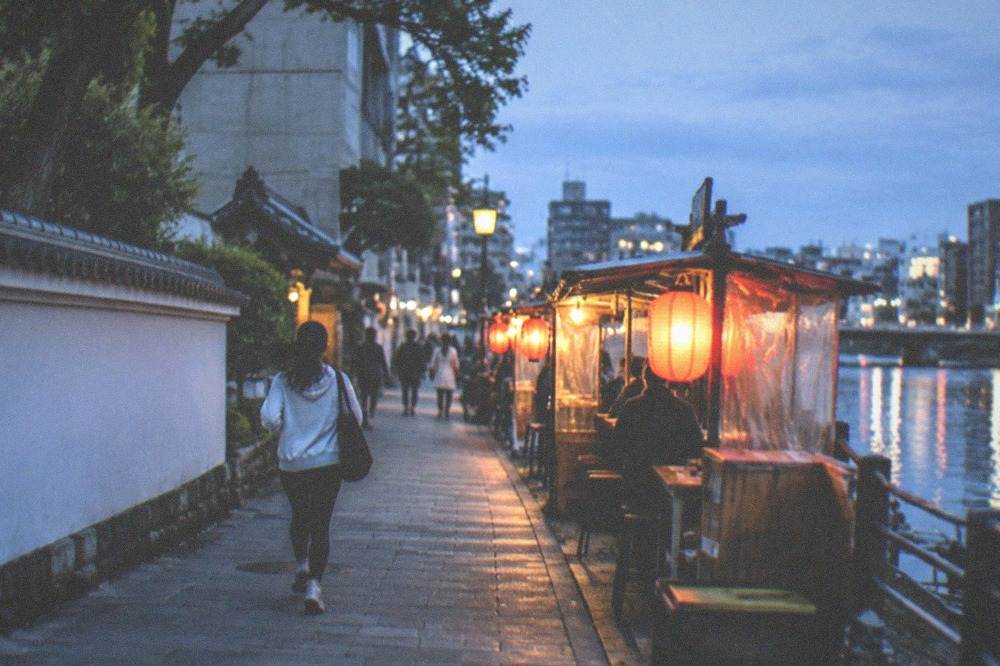 A row of lantern-lit food stalls beside a river at night in Fukuoka.