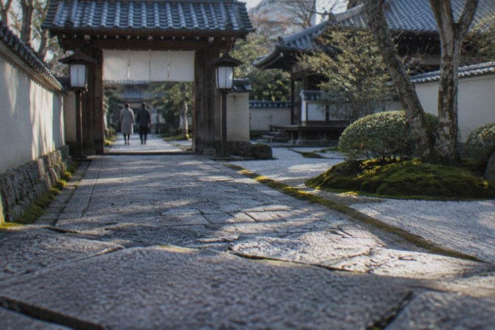 Stone paved approach to a small Zen temple gate with lanterns and moss