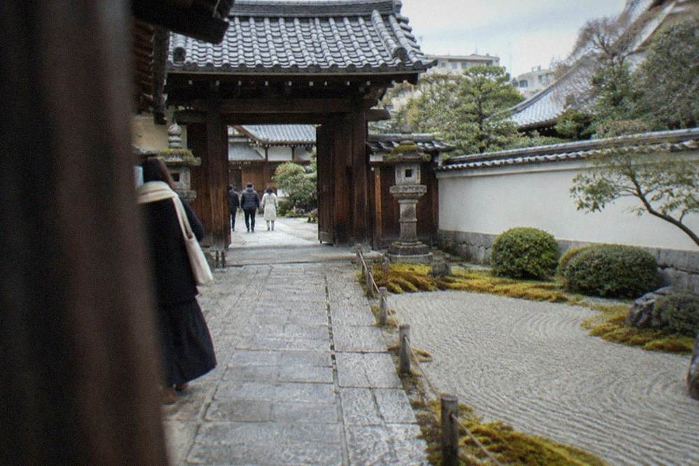 Wooden temple gate under tiled roof with stone lanterns at its base
