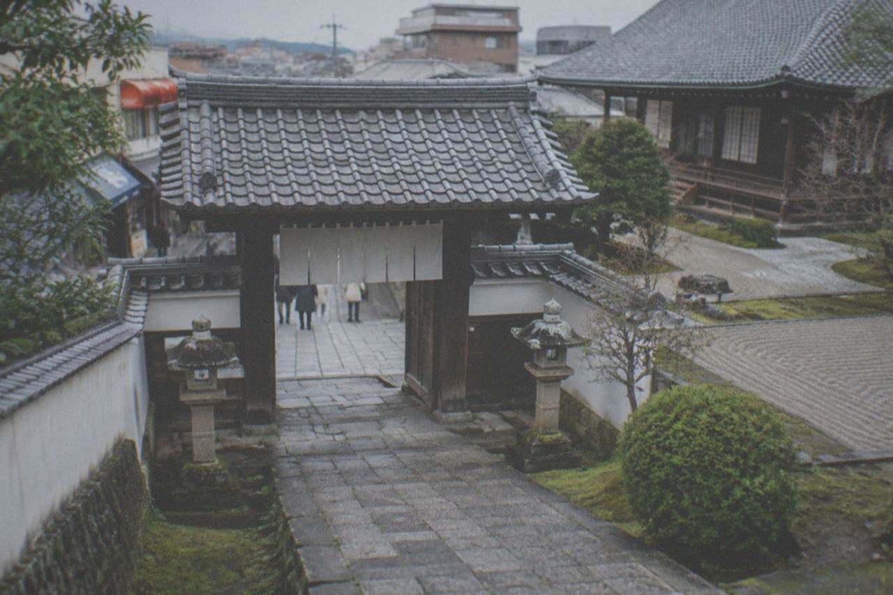 Stone paved approach to a small Zen temple gate with lanterns and moss