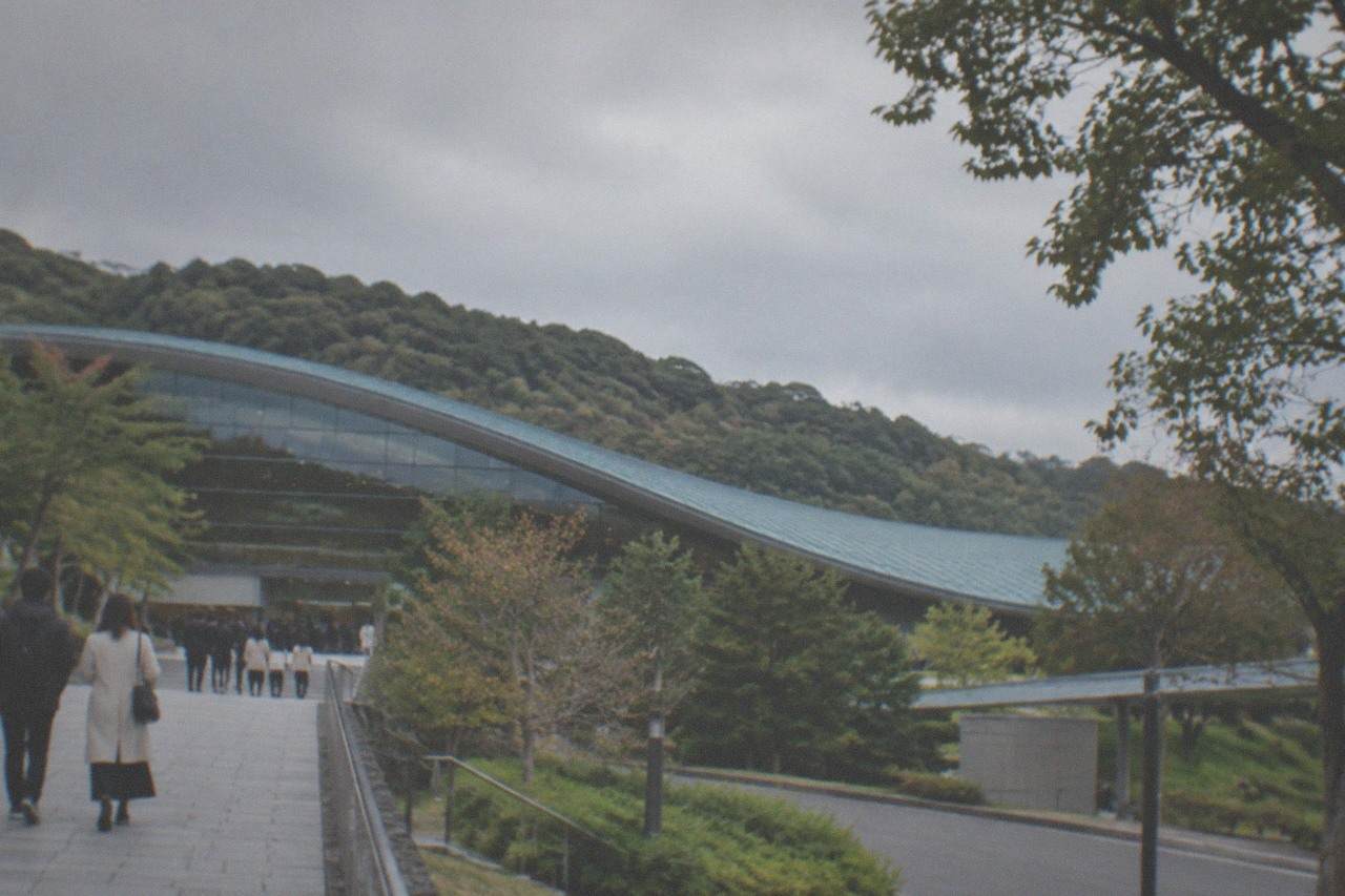 Large modern museum building with a sweeping curved roof set against forested hills