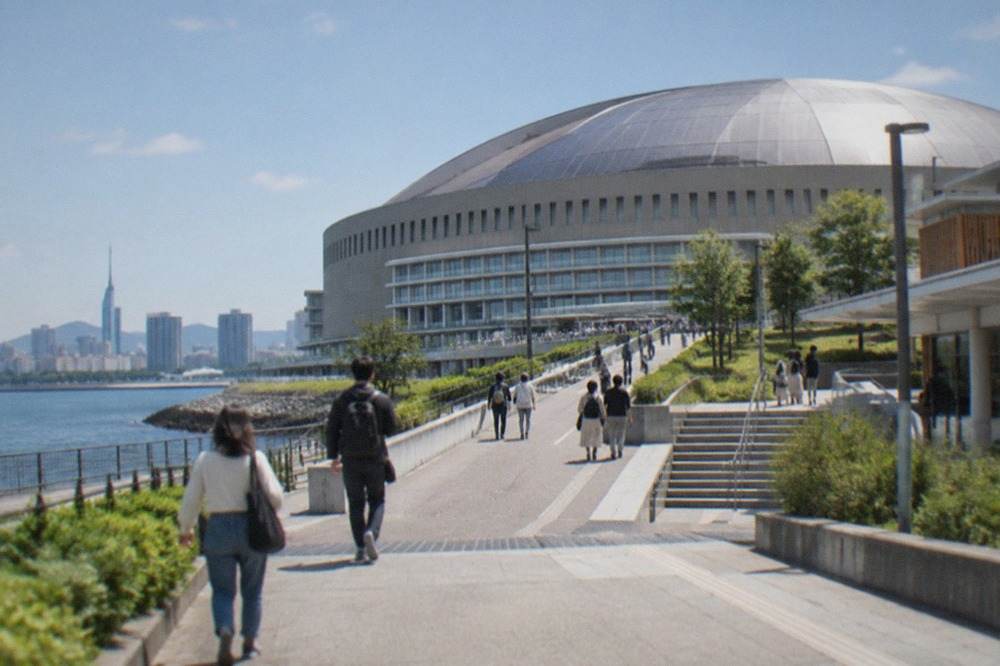 A large domed stadium beside a bay with high-rise buildings behind it