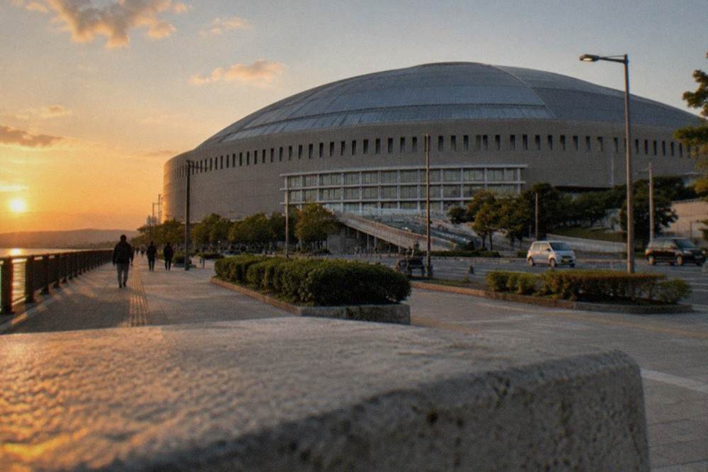 The curved roof of a domed stadium seen from a seaside boulevard at dusk
