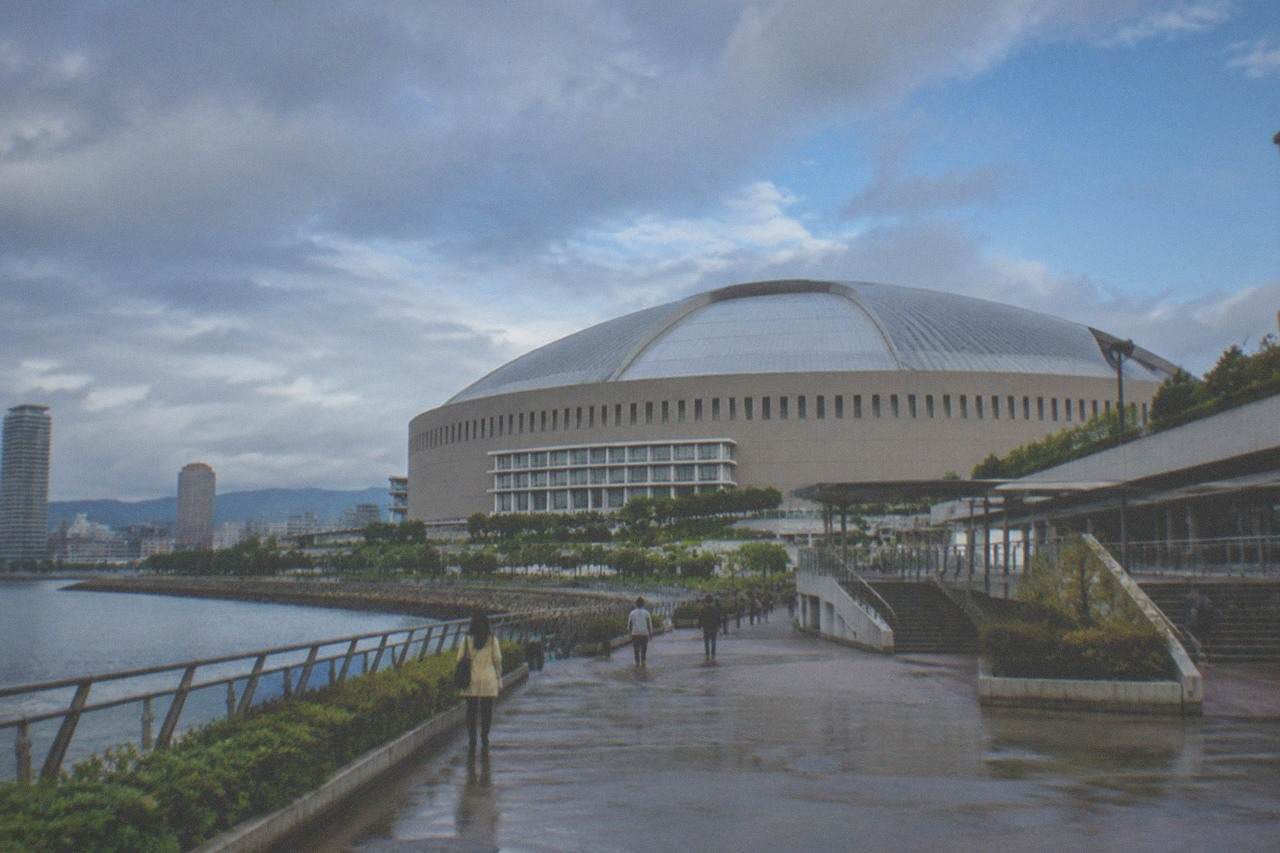 A large domed stadium beside a bay with high-rise buildings behind it