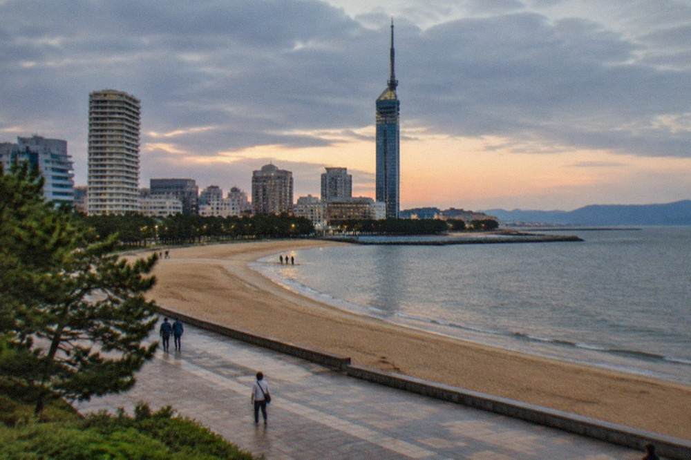 Seaside tower lit up at dusk above a wide promenade