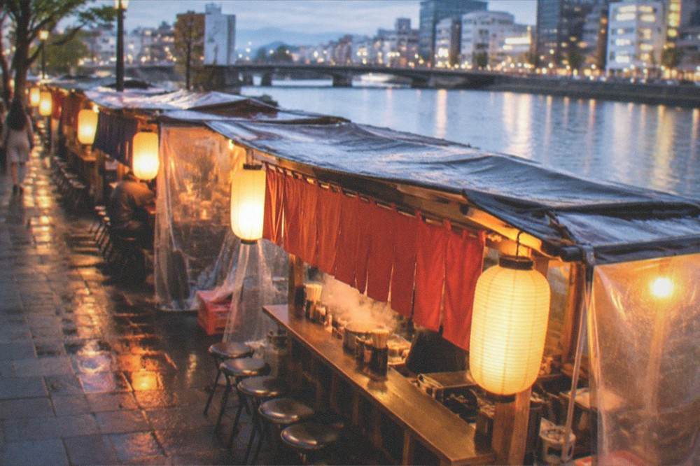 Night street beside a river with lantern light spilling from small food carts onto the pavement